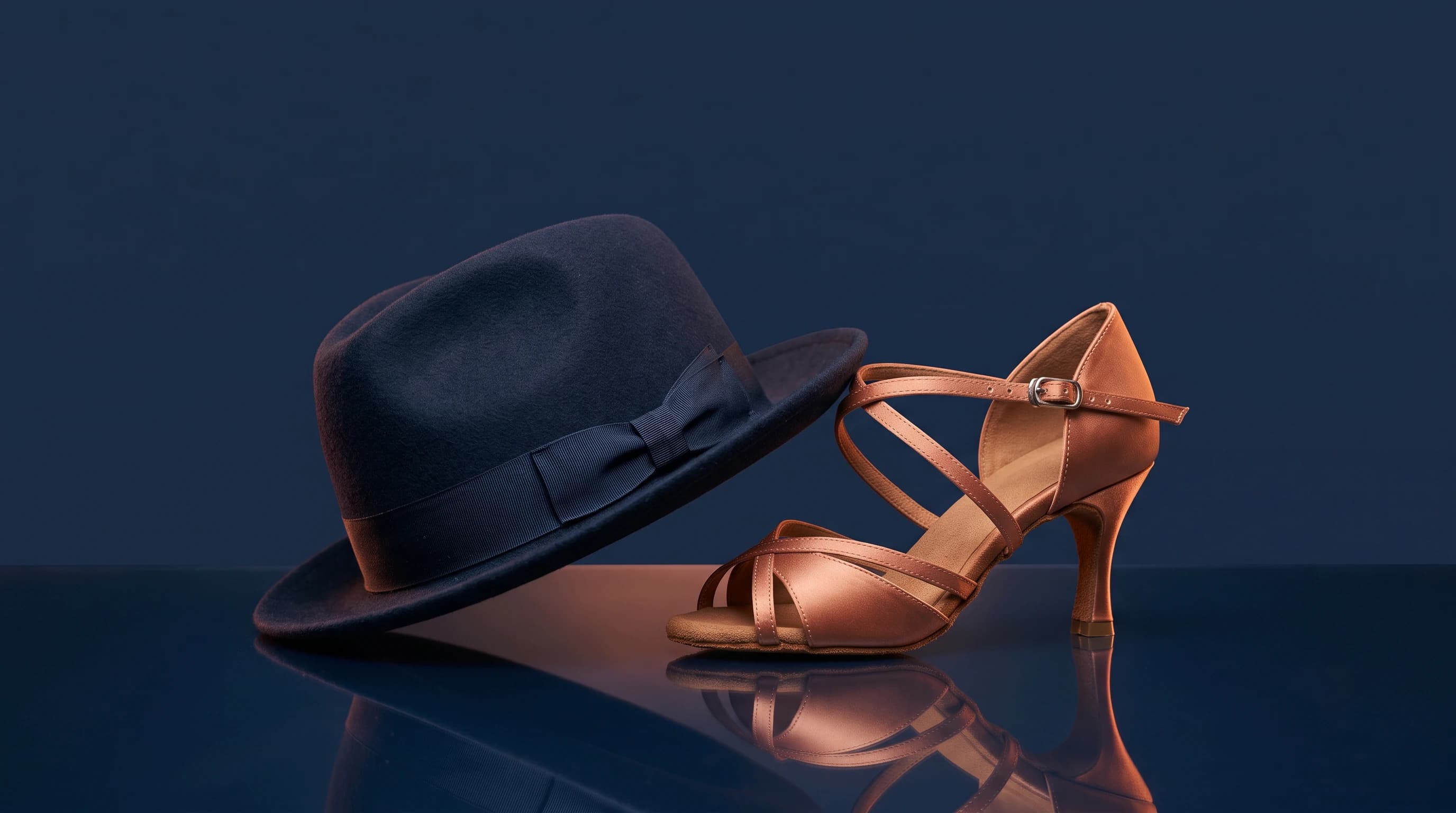 Un chapeau feutre bleu nuit et un escarpin de danse cuivré réunis sur un fond bleu nuit
